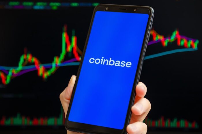 Coinbase mobile app running at smartphone screen with trading candlestick chart at background.