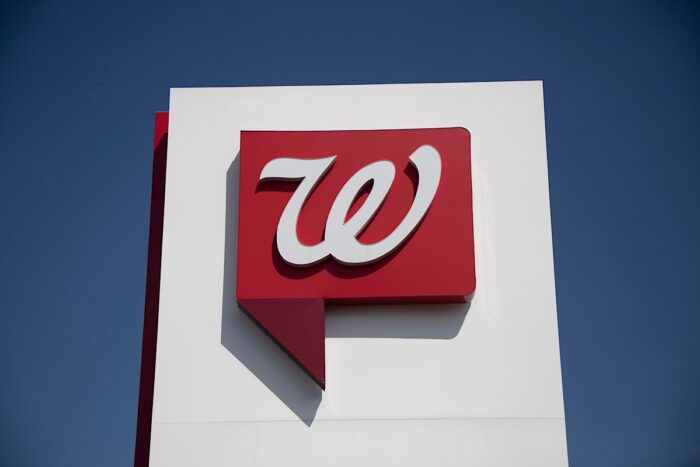 Close up of Walgreens logo signage against a blue sky.