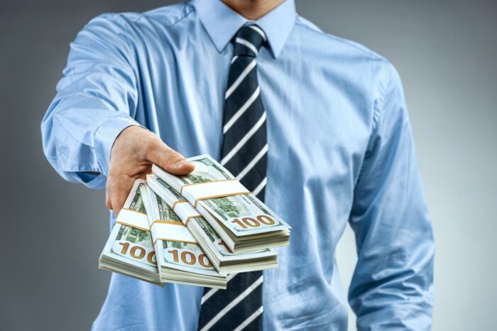 Man in blue shirt holding cash of one hundred dollars. ftc checks