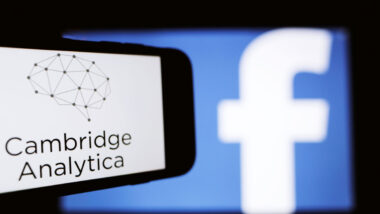 The logo of the strategic communication company Cambridge Analytica is seen on the screen of an iPhone in front of a computer screen showing Facebook logo.