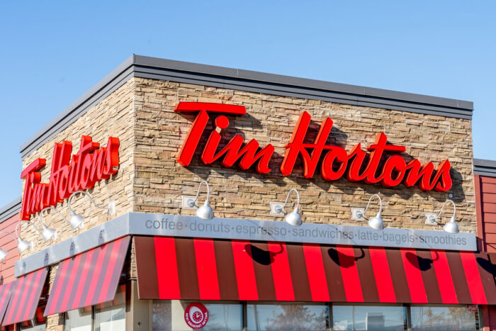 Close up of Tim Hortons signage on exterior of building against a blue sky.