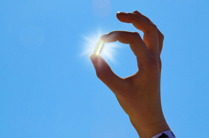 Young Woman is holding Vitamin D Capsule against the sun and blue sky.