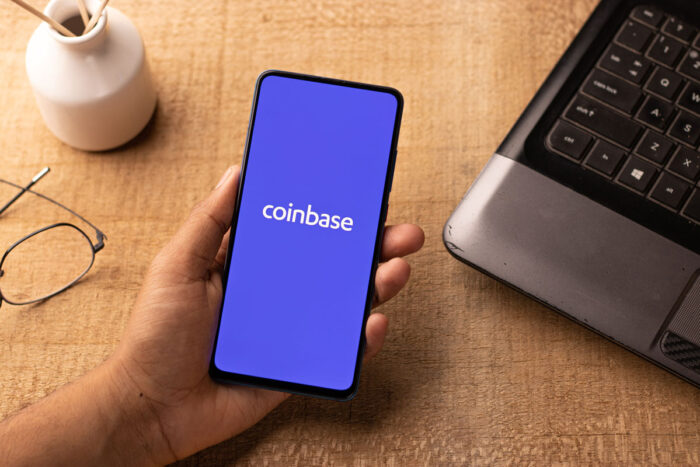Hand holding a smartphone with Coinbase logo on the screen.
