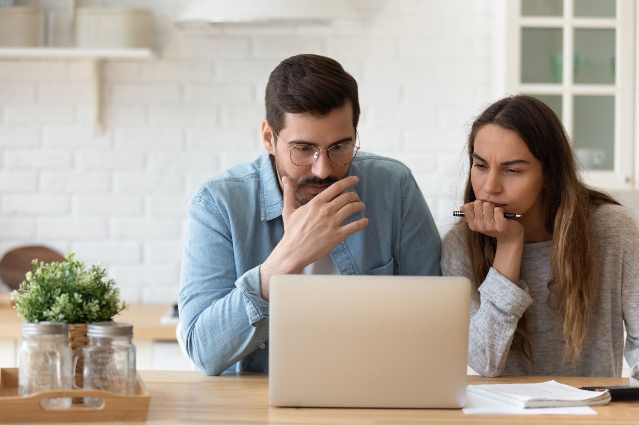 Serious concerned married couple sit indoor looking at laptop receive notification from bank