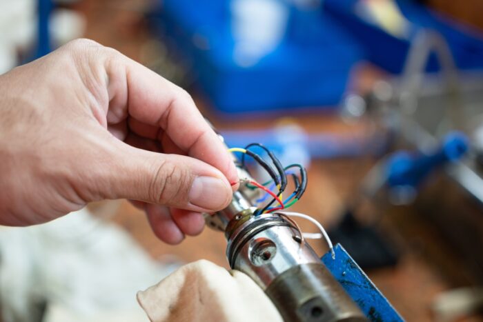 An electrician's hand is choosing the electricity wire of electronic equipment. Industrial working scene, close-up and selective focus - wage-and-hour class action