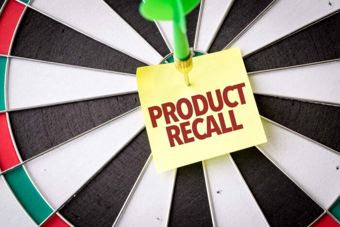 Close up of a dart on a dart board holding a sticky note that reads: product recall.