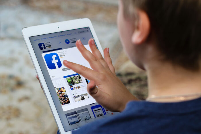 Boy teenager installs a program of the social network Facebook on iPad Air Apple from iTunes.