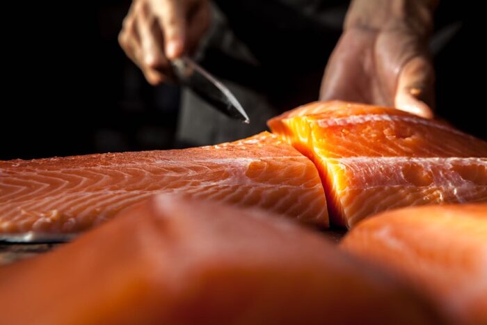 Close up of a chef cutting a large raw salmon fish.