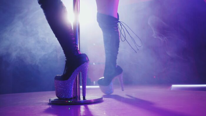 woman in high boots on platform and heel with rhinestones. Fringe skirt with pendants made of shiny stones. striptease dancer moving on stage in strip night club - Deja Vu Services settlement, class action lawsuit settlement