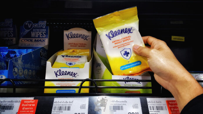Man's hands are holding wet tissue (Brand "Kleenex") stacked on a shelf in a supermarket.