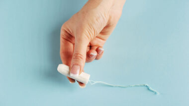 Hygienic tampon between the fingers of the female hand. Blue background. Close-up.