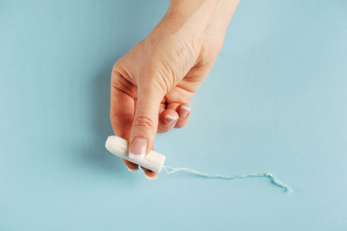 Hygienic tampon between the fingers of the female hand. Blue background. Close-up.