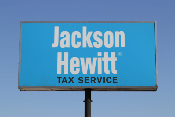 Close up of Jackson Hewitt on a billboard sign against a blue sky.