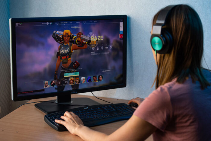 Girl playing Valorant video game on PC. Valorant is an online shooter game developed by Riot Games - discrimination settlement