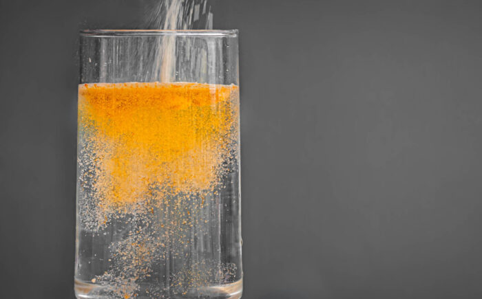 Powered orange drink mix being poured into a clear glass of water.