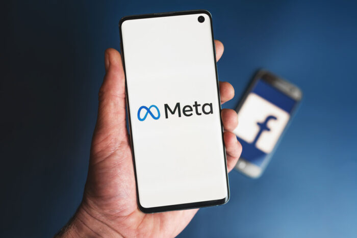 META logo on smartphone being held in hand in front of phone with Facebook icon.