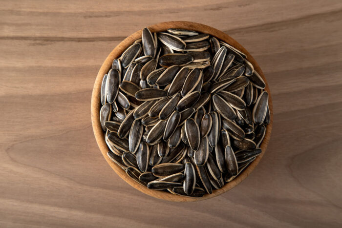 Black sunflower seeds in a bowl on wooden background.