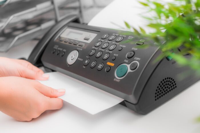 A person pulls a paper from a fax machine in an office - Best Doctors Settlement
