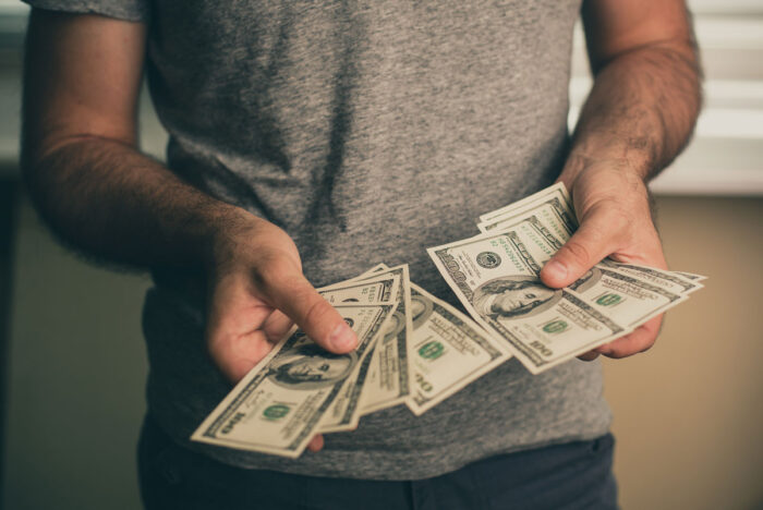 Close up of a mans hands holding one hundred dollar bills. Class action rebate concept.