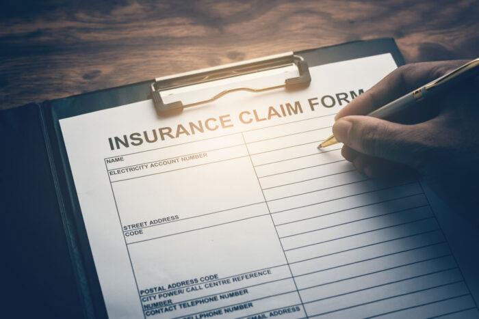 Hand with pen on application form for registering claim for insurance - state auto insurance lawsuit, underpaid insurance claims