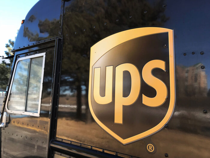 The side of a UPS delivery truck parked at a building as the driver makes deliveries.