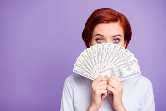 Woman holding settlement payment money in front of face 