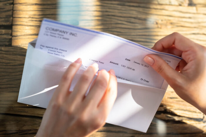 Close up of hands opening an envelope with a money check inside - root insurance lawsuit