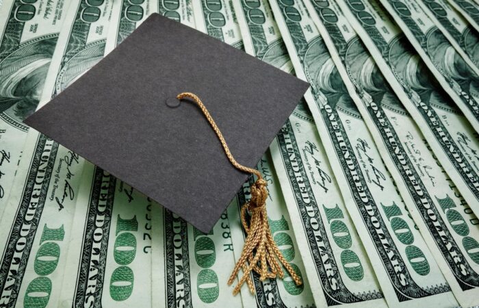 Close up of a graduation cap on top of one hundred dollar bills.