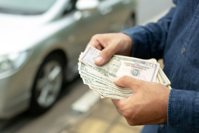 Close up of a mans hands holding money in front of a car, representing the Permanent General Assurance, or PGAC, settlement