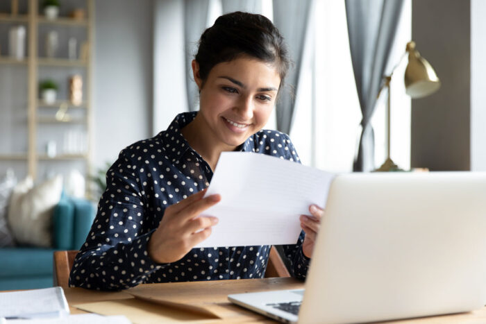 Photo of a young woman smiling while looking at a class action rebate check she received in the mail.