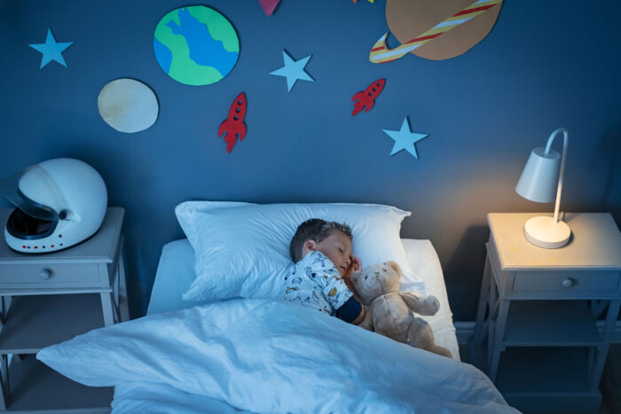 Boy sleeping in a bed after taking melatonin in a space decorated room.