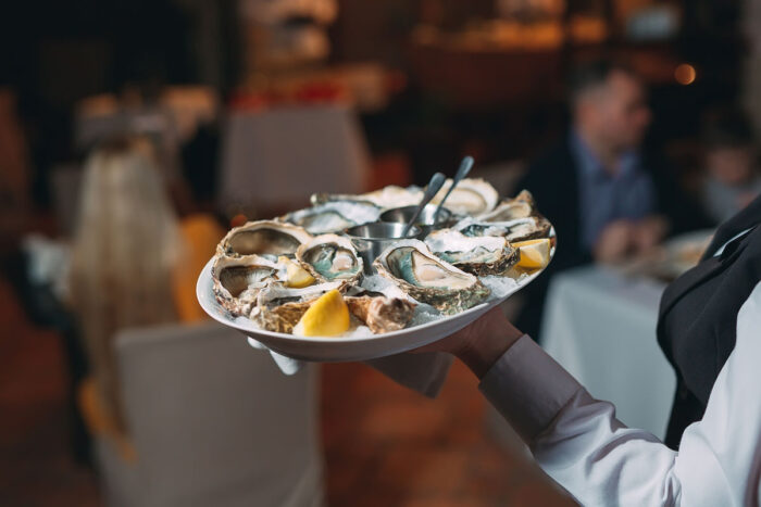 Close up of a food workers hand serving a tray of oysters - King’s Seafood data breach settlement