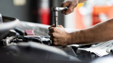 Close up of a mans hands using a tool to fix the engine of a car.