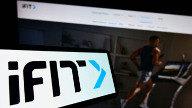 Mobile phone with logo of American fitness company iFIT Inc. on screen in front of business website.