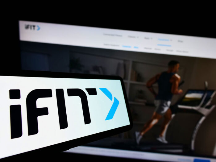 Mobile phone with logo of American fitness company iFIT Inc. on screen in front of business website.