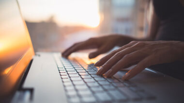 Close up of a womans hands typing on a laptop keyboard.
