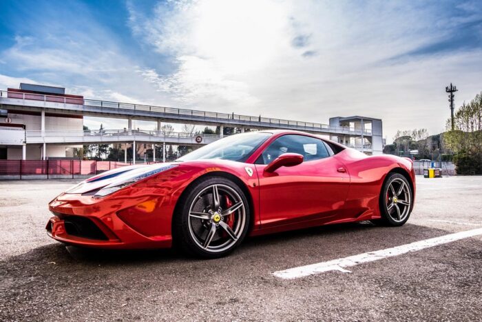 Ferrari supercar in a parking lot against a bright blue sky.