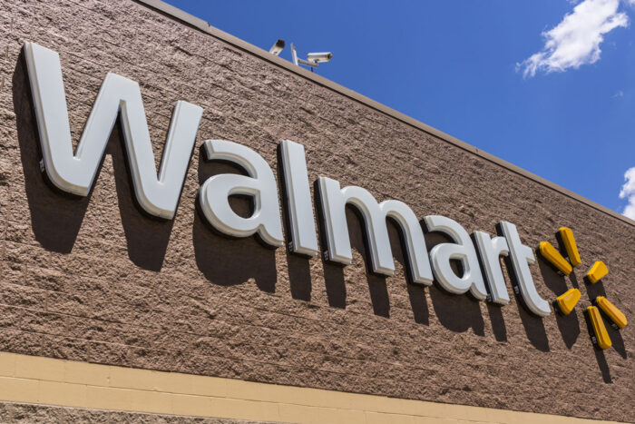 Close up of Walmart signage on exterior of building against a blue sky.