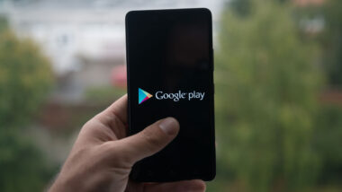 Man holding smartphone with Google play store logo with the finger on the screen.