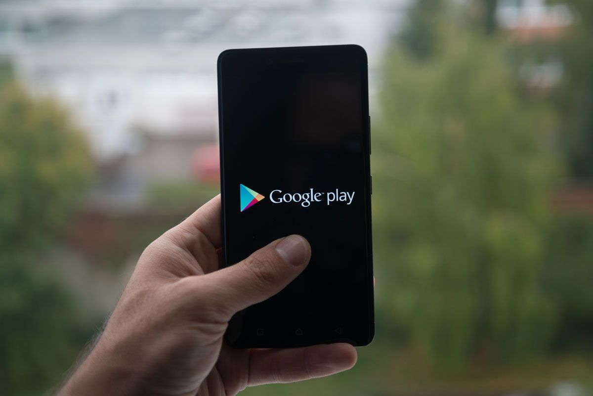 Man holding smartphone with Google play store logo with the finger on the screen.