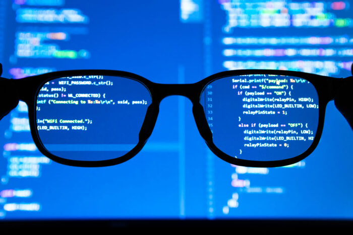 Silhouette glasses in front of laptop computer screen with programming code.