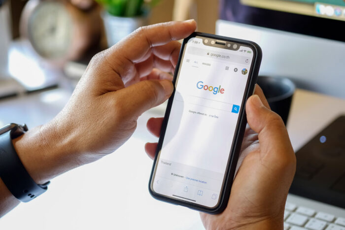 Close up of a mans hands holding a smartphone with Google homepage displayed on screen.