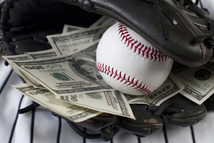 Close up of a baseball and money notes inside of a baseball mitt, representing the MLB settlement.