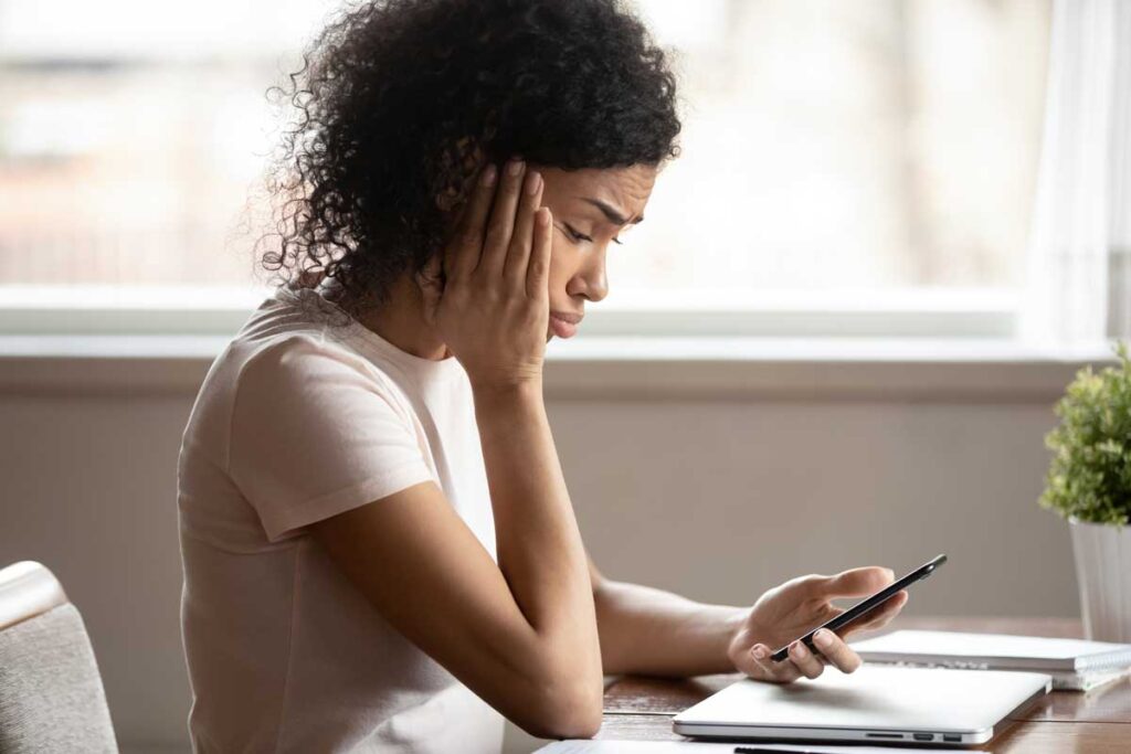 Mixed race 30s woman pouted lips looking at smartphone frustrated by received sms or notification, representing the Sunshine and Life Health Advisors marketing texts settlement.