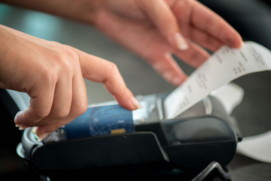 Close up of a womans hands grabbing a receipt from a point of sale terminal, representing the Hibbett class action lawsuit settlement.