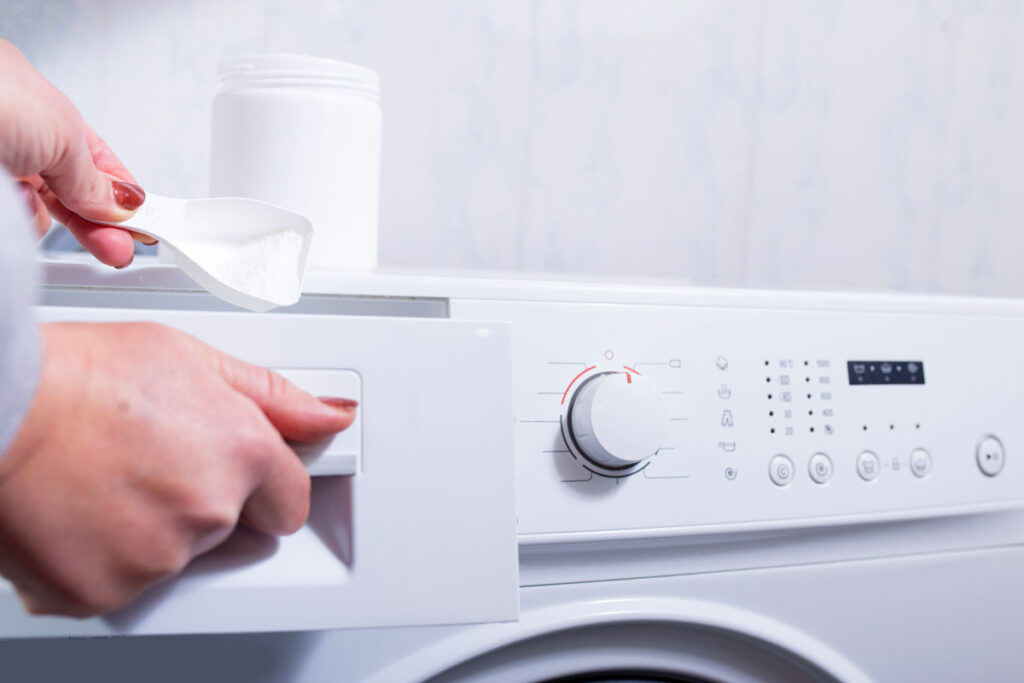 Close up of a womans hands putting laundry detergent in a washer.