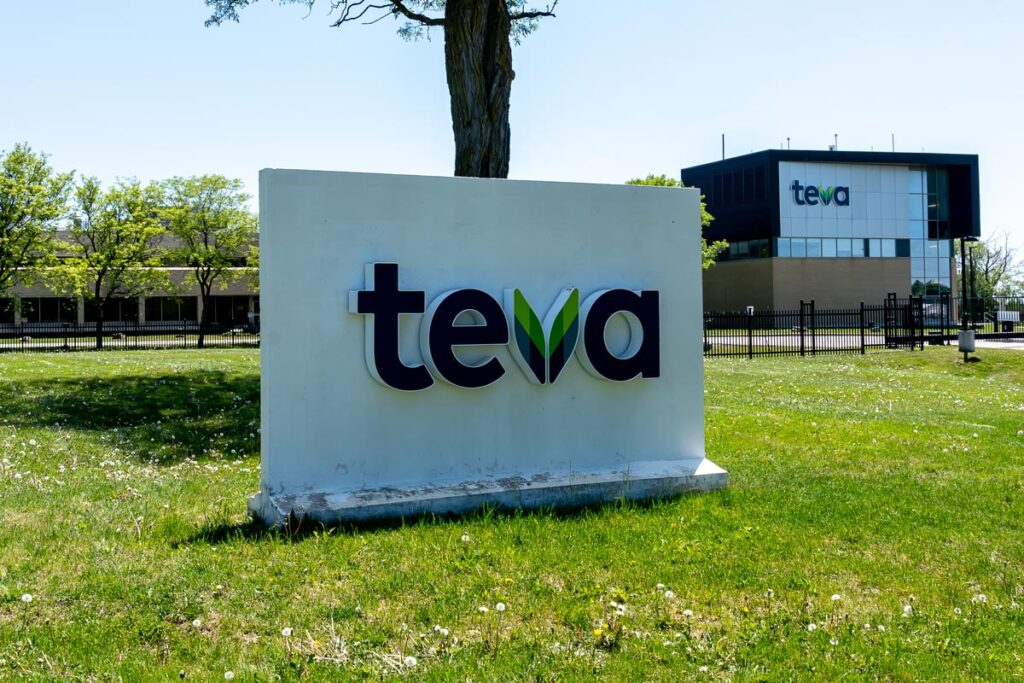 Close up of Teva signage in a grass field against a blue sky.