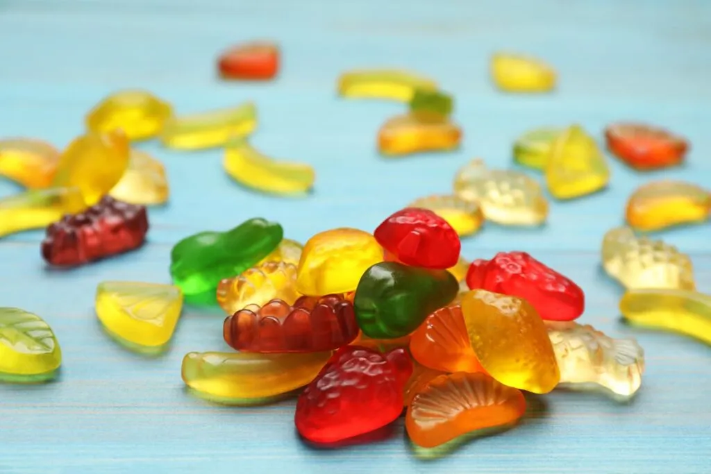 Delicious gummy fruit shaped candies on light blue wooden table, closeup.