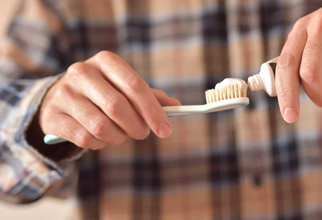 Close up of a mans hands putting toothpaste on a toothbrush.