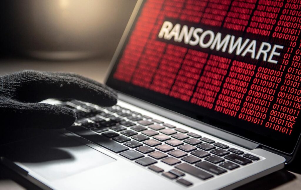 Male hacker hand on laptop computer keyboard with red binary screen of ransomware attacking, representing the Morley Companies data breach class action lawsuit settlement.